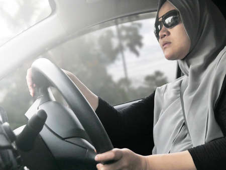 Portrait of young Asian muslim woman smiling and driving a car, good looking entrepreneur, car sharing conceptの写真素材