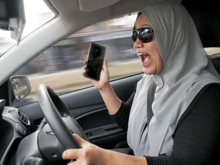 Female Asian muslim driver making a call while driving a car, dangerous traffic safety accident...
