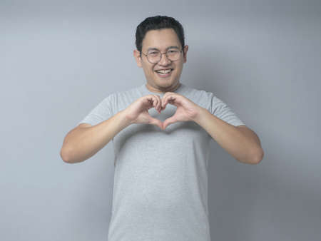 Portrait of young Asian man Smiling happily while showing love sign with hand gestureの写真素材