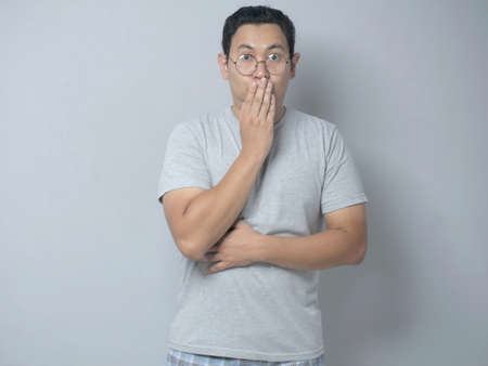 Close up portrait of attractive Asian young man closing his mouth with fingers. Worried gesture, can't say anything. Shocked surprised to hear bad news or gossip, looking at cameraの写真素材