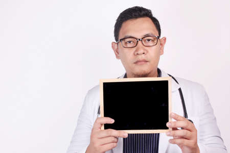 Male doctor wearing white coat and stethoscope holding and showing empty blackboard, copy spaceの写真素材