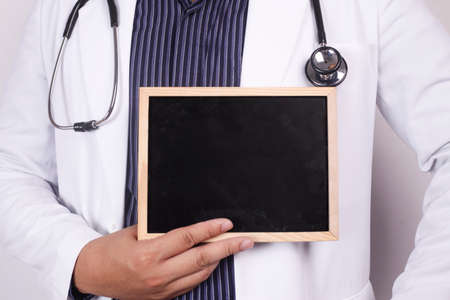 Male doctor wearing white coat and stethoscope holding and showing empty blackboard, copy spaceの写真素材