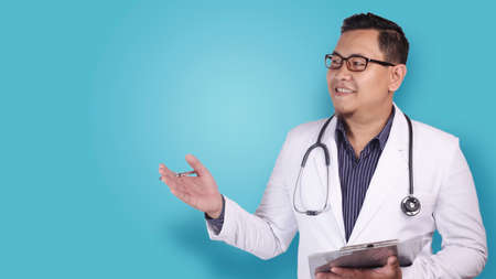 Portrait of Asian male doctor wearing white coat and stethoscope, presenting something on his side with copy spaceの写真素材
