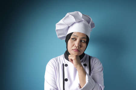 Portrait of Asian woman chef thinking gesture against blue backgroundの写真素材