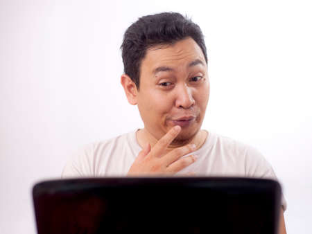 Portrait of young funny Asian man smiling naughty when looking at his laptop, watching porn online