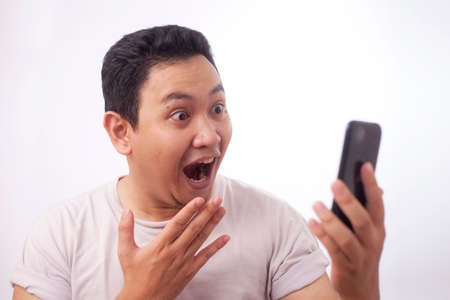 Portrait of happy funny Asian man shocked or surprised with mouth open, good news on smart phone...
