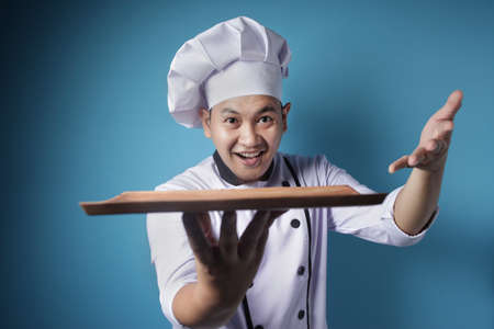 Portrait of Asian male chef looks happy and proud presenting something on his empty wooden plate, copy space meal menu conceptの写真素材