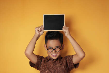 Portrait of smart young cute Asian boy smiling at camera while holding and showing empty blackboard...