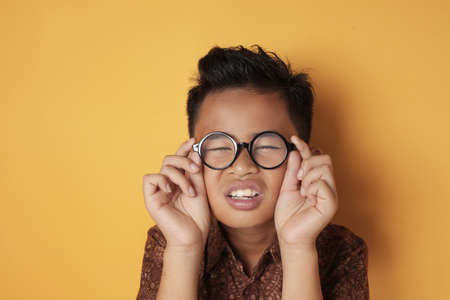 Portrait of Asian boy adjusting his eye glasses, sight problem concept, against yellow backgroundの写真素材