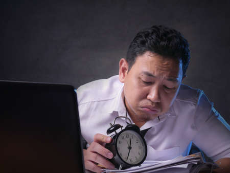 Young Asian businessman worried by time when looking at a clock. Work deadline stress at the officeの写真素材