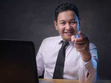 Portrait of young Asian man pointing forward, looking at camera. Choosing someone concept with selective focusの写真素材
