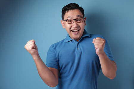 Portrait of a funny young Asian man dancing happily joyful expressing celebrating good news victory...
