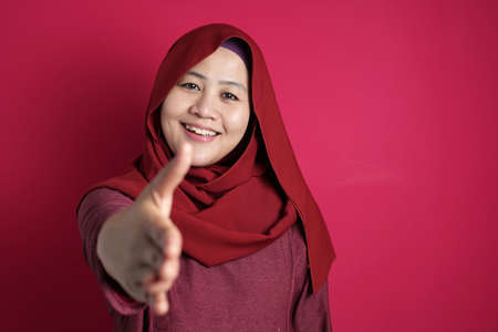 Portrait of muslim businesswoman offers hand shake, deal partnership agreeement concept, selective focus image against red backgroundの写真素材