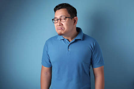 Portrait of arrogant young Asian man standing and shows upset cynically annoyed gesture, against ...