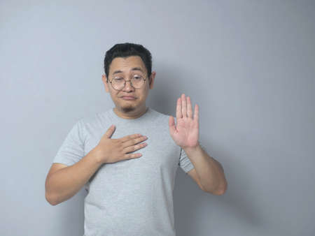Portrait of happy Asian man making pledge gesture, hand on chest holding heart, making promise