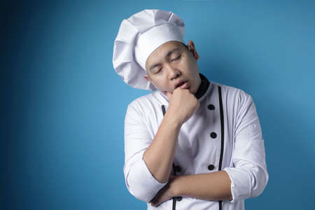Portrait of tired sleepy Asian chef, too much working in the kitchen, hard pressure on restaurant culinary industry concept, against blue backgroundの写真素材
