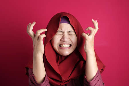 Portrait of Asian muslim lady wearing hijab shows angry screaming gesture, against red backgroundの写真素材