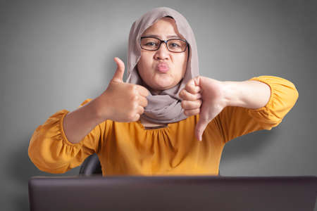 Portrait of Asian muslim businesswoman shows thumbs up and down gesture, concept of good and bad decision conceptの写真素材