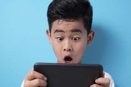 Asian boy shocked when looking at his tablet, kid surprised to see something on internet