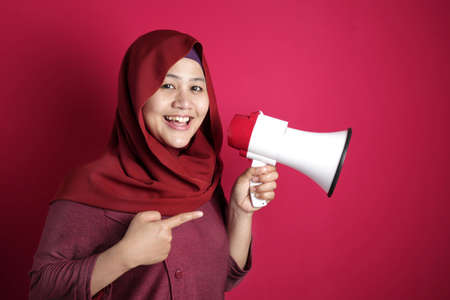 Young Asian woman wearing hijab shouting with megaphone, side view. Leader or supporter concept....