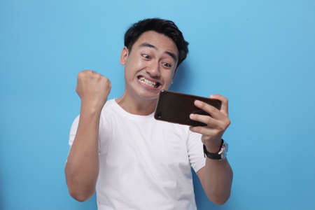 Portrait of a cute handsome young Asian man with funny face playing games on tablet, winning expressionの写真素材