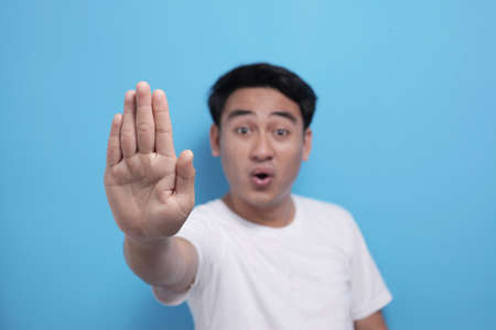 Portrait of young Asian man shows stop gesture with his finger against blue background