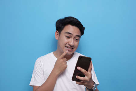 Attractive young Asian man wearing reading texting chatting on his phone, bad news, sad shocked...