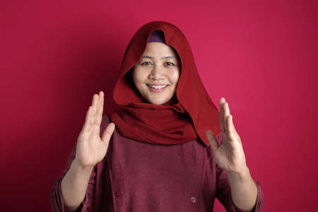 Portrait of Asian young happy muslim woman  presenting something between her hands, against red...