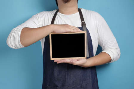 Portrait of Asian male chef or waiter looks happy and proud showing empty blackboard, presenting blank writing template, copy space meal menu conceptの写真素材