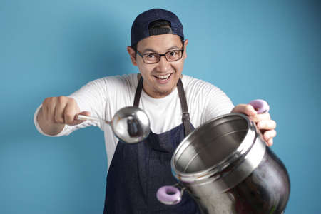 Portrait of Asian male chef smiling happy while holding kitchen tools, chef holding pot and ladle...