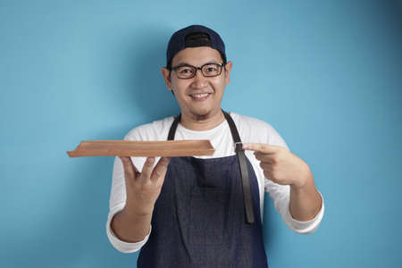 Portrait of Asian male chef or waiter looks happy and proud presenting something on his empty wooden...