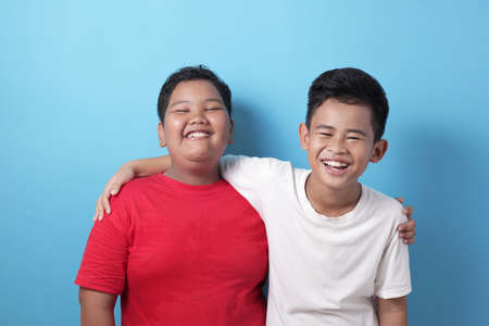 Two Asian boys looking at camera, smiling and laughing, best friend relations between two young kid,...