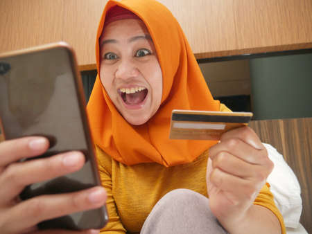 Happy Asian muslim woman wearing hijab smiling and laughing, thinking of good things when making...