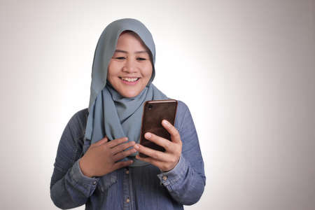 Portrait of young Asian muslim woman wearing hijab get good news on her phone, happy surprised expressionのeditorial素材