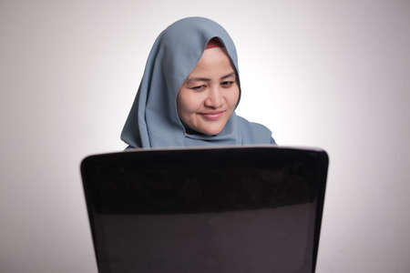 Portrait of Asian muslim woman with cunning look working on laptop, hacker internet criminal conceptのeditorial素材