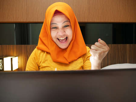 Portrait of Asian muslim lady shows happy surprised expression celebrating winning victory gesture...