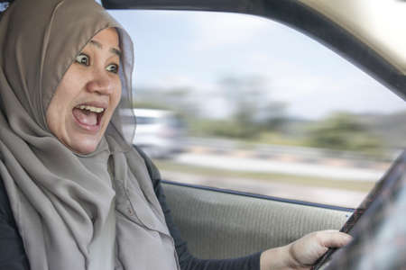 Portrait of female Asian muslim driver shocked and panic about to have crash accident, zoomed motion...