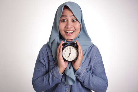 Young Asian muslim woman wearing hijab holding a clock, smiling expression, on time management...
