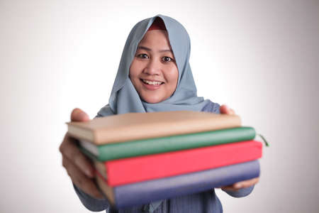 Portrait of cute friendly smiling muslim lady offering book to readの写真素材