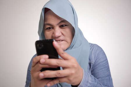 Portrait of beautiful young Asian muslim woman angry when reading bad news text message on her smart...