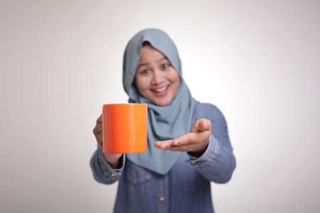 Portrait of happy young beautiful Asian muslim woman smiling, drinking tea or coffe during coffee breakの写真素材