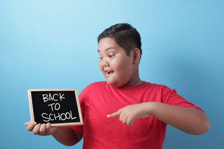 Happy smiling Asian boy student holding blackboard with back to school words written on it