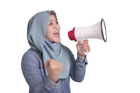 Young Asian muslim woman wearing hijab shouting with megaphone and pointing to camera. Leader supporter or protester concept. Close up body portraitの写真素材
