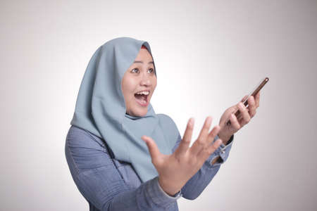 Portrait of Asian muslim woman surprised and smiling happy to see something above when using her...