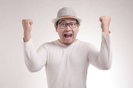 Portrait of successful young Asian businessman shows winning gesture, celebrating victory. Hands raised aboveの写真素材