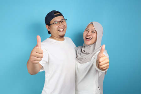 Portait of happy Asian muslim couple smiling and shows thumbs up gesture, husband and wife hugging...