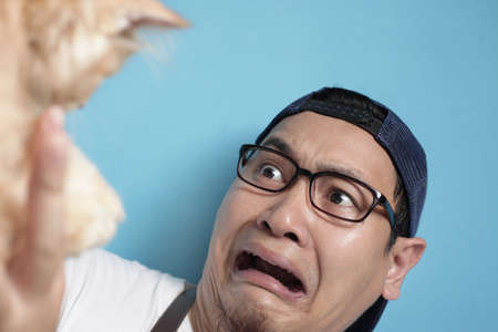 Man afraid of cat, funny face of a young Asian male scared or intimidated by kitten, cat allergy...