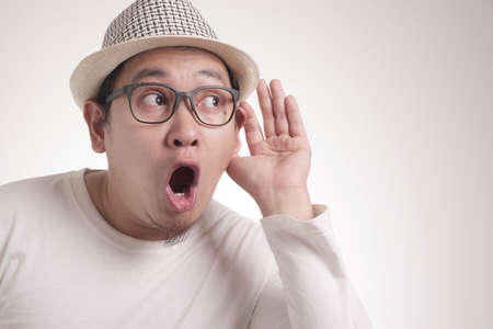 Young asian men wearing blue shirt listen whispers with funny face. Curious. Intently listen in on...