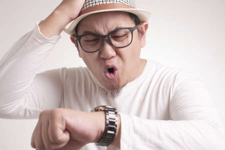 Young Asian man worried by time when looking at his wristwatch. Work or school time deadline