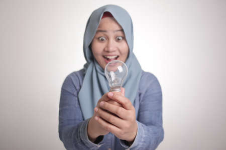 Asian muslim woman holds lamp bulb with smiling happy expression, idea concept with selective focusの写真素材